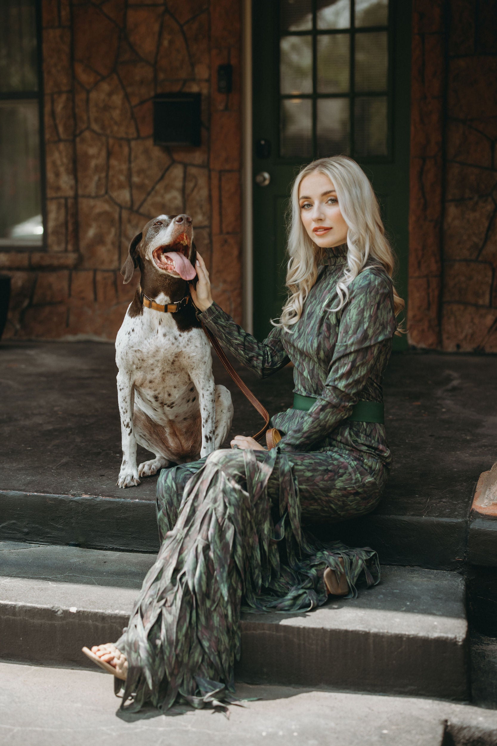 Woman in a stylish green dress sitting with a dog on porch steps, showcasing elegant Texas fashion.