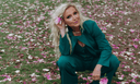 Woman in a teal suit posing with a flower in her hair amidst pink flower petals.