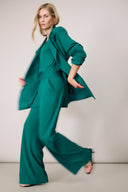 Woman in a stylish green suit, striking a dynamic pose against a neutral background.