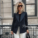 Woman in a black blazer and white pants walking on a city street.