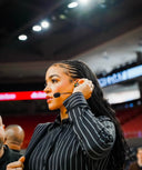 Andraya Carter, ESPN basketball analyst, adjusts her earpiece during a sports event, showcasing her stylish look.