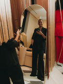 Fashion Designer, Carly Cushnie posing in front of a mirror wearing a stylish black suit.
