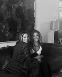 Editor in Chief, Cristina Cuomo with a friend posing on a sofa in a stylish interior setting.