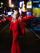 Comedian, Soo Ra in a vibrant red suit, posing confidently on a city street at night.