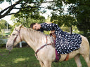 Woman in Sexy Day leaning on a white horse under a tree, enjoying a sunny outdoor moment.