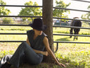 Woman in Supernova sitting by a tree near a horse, enjoying a sunny day outdoors.