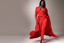 Confident woman in a striking red outfit, elegantly walking with a flowing train, showcasing fashion style.