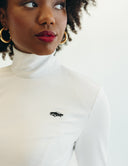 Woman wearing a white mock neck top with a black car emblem, showcasing a stylish and modern look.