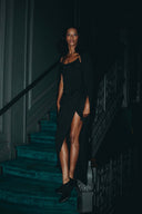 Model wearing the Come Closer dress on a staircase, showcasing its elegant asymmetrical silhouette and high split-leg.