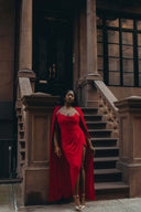 Come Closer dress featuring a red asymmetrical silhouette, ruched neckline, and high split-leg look with optional cape.