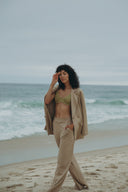 Model in a Dahlia Blazer, styled with beachwear, standing on the shore with waves in the background.
