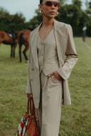 Model wearing Dahlia Blazer in beige, paired with matching vest and pants, showcasing style and elegance outdoors.