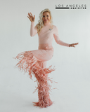 Woman in vibrant pink fringe outfit striking a joyful pose against a white background, showcasing trendy fashion.