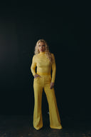 Stylish woman in a bright yellow jumpsuit posing against a dark background, showcasing modern fashion trends.