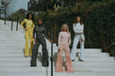 Four women in stylish outfits pose on outdoor stairs, showcasing trendy fashion and diverse styles during a photoshoot.