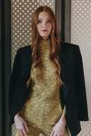 Model in a stylish black blazer and golden dress, posing confidently against a patterned backdrop.