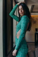Model in a green, long-sleeve dress with cutouts, striking a pose indoors against a stylish backdrop.