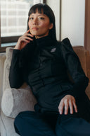 Woman in a sleek black dress sitting on a sofa, exuding elegance with a thoughtful pose.