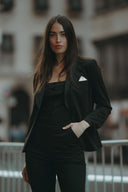 Confident woman in black suit posing outdoors with a sleek hairstyle and stylish attire.