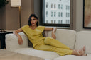Woman in a stylish yellow outfit lounging on a sofa near a window with urban views.