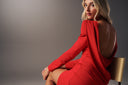 Woman in a stunning red dress with an open back, seated gracefully in a modern setting.