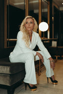 Woman in the Meet me At Noon set sitting elegantly on a couch in a stylish interior, spotlighted by a modern lamp.