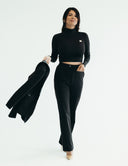 Woman in a stylish black three-piece suit with a fitted top, holding a blazer, exuding elegance and comfort.