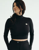 Model showcasing a cropped black long sleeve top with a fitted silhouette, styled with a high-waisted suit pant.