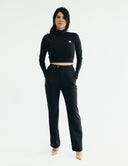 Confident woman in a black cropped top and high-waisted suit pants, showcasing a stylish and comfortable three-piece suit.