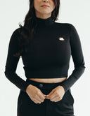 Model wearing a fitted black cropped top with long sleeves and a unique tea cup pin, showcasing a stylish yet comfortable look.