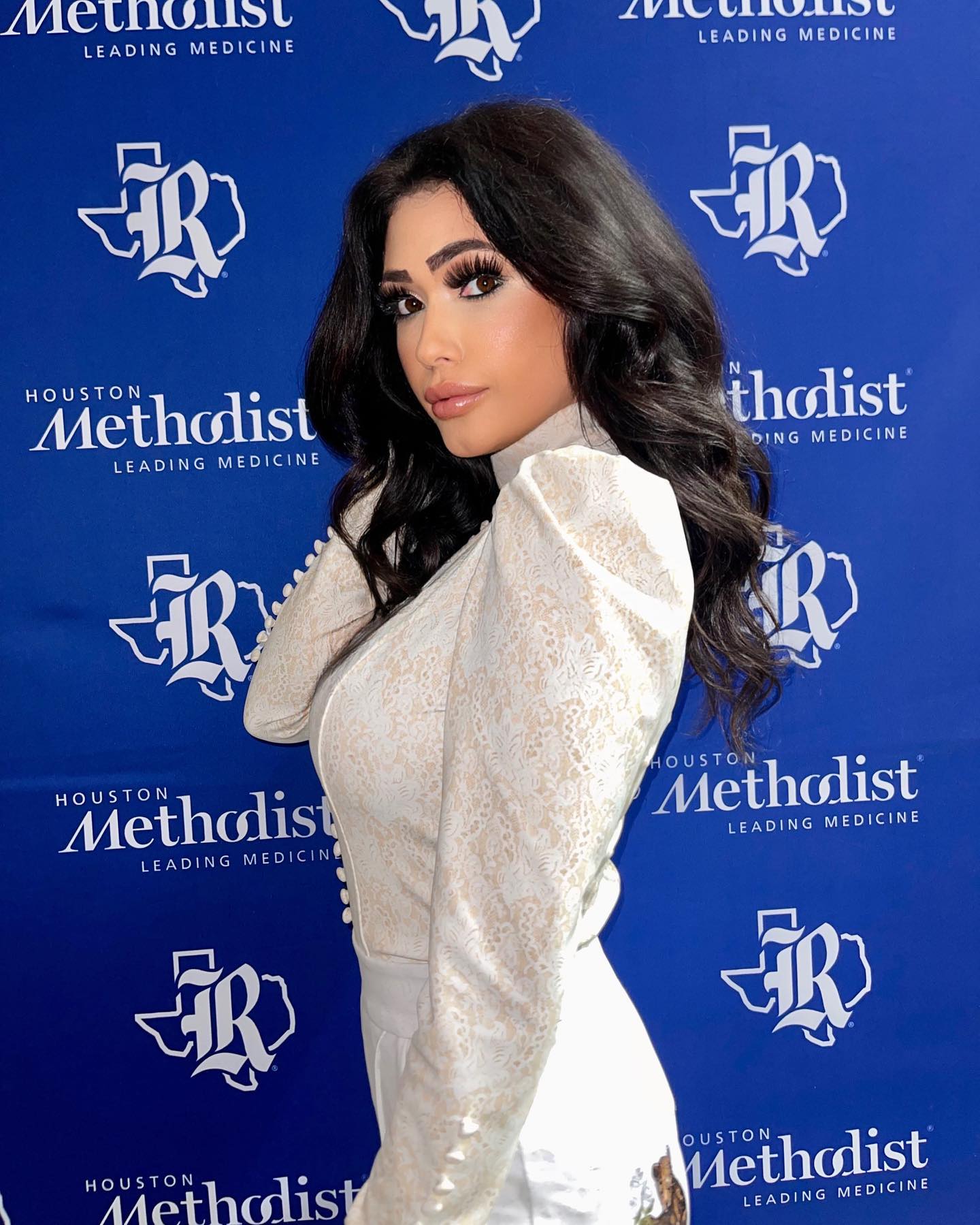 Woman in I Do poses against Houston Methodist backdrop, showcasing elegance and confidence at an event.