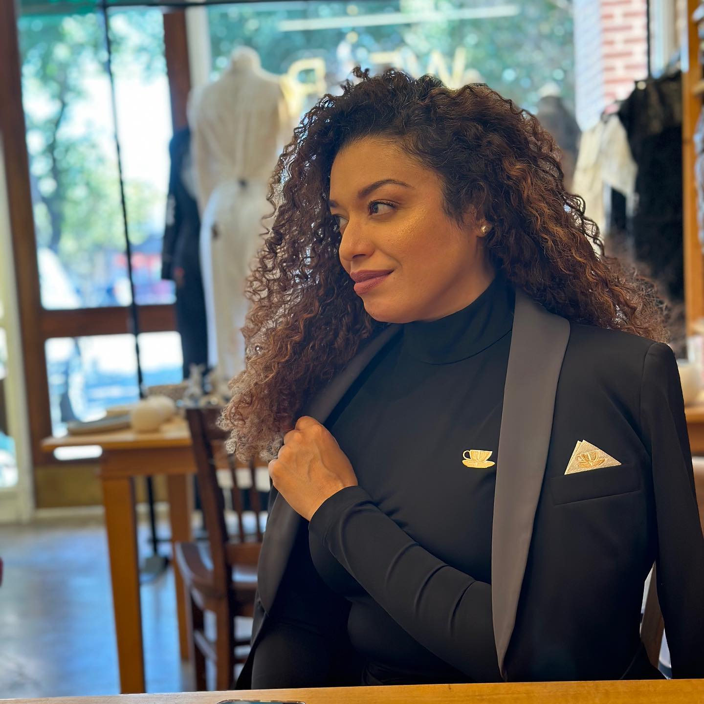 Woman with curly hair in Tea Time Set seated at a cafe, showcasing elegance and confidence.