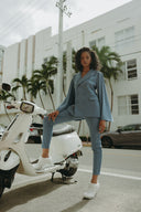 Woman in a blue suit poses confidently next to a vintage scooter in an urban setting.