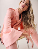 Model wearing a Cool Intentions Blazer with batwing sleeves and satin lapels, stylishly posed on a chair.