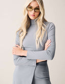 Cut to the Chase Top in light gray, featuring a high neck and asymmetrical design, paired with stylish glasses.