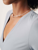 Close-up of a model wearing the Luxe Long Sleeve Bodysuit with a silver necklace and a scoop neckline.