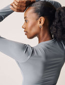 Model showcases the Luxe Long Sleeve Bodysuit in a side view with elegant styling and natural lighting.