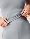 Close-up of a model adjusting the Luxe Tank Top in gray, showcasing its sleek fabric and fit.