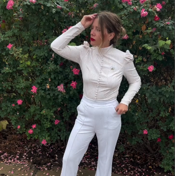 Young woman in I Do jumpsuit poses against a backdrop of pink roses, showcasing contemporary fashion and floral beauty.