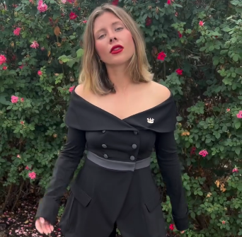 Woman in Tux All Day/All Night set with red lipstick standing in front of flowering greenery.