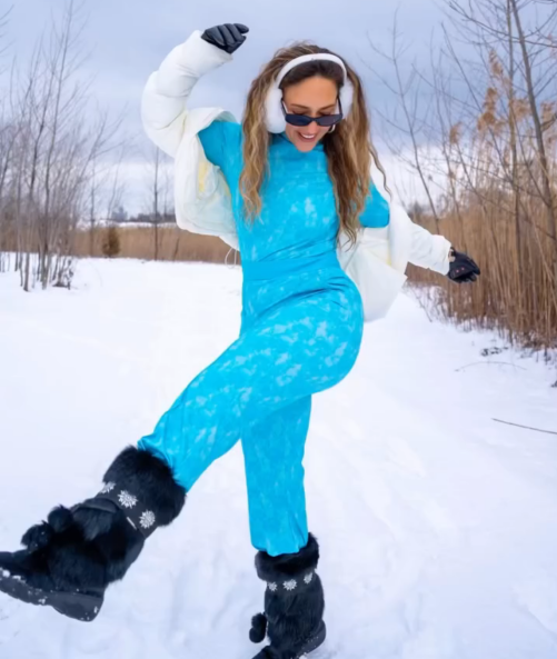 Woman in Fellini joyfully in snowy landscape, wearing earmuffs and stylish boots.