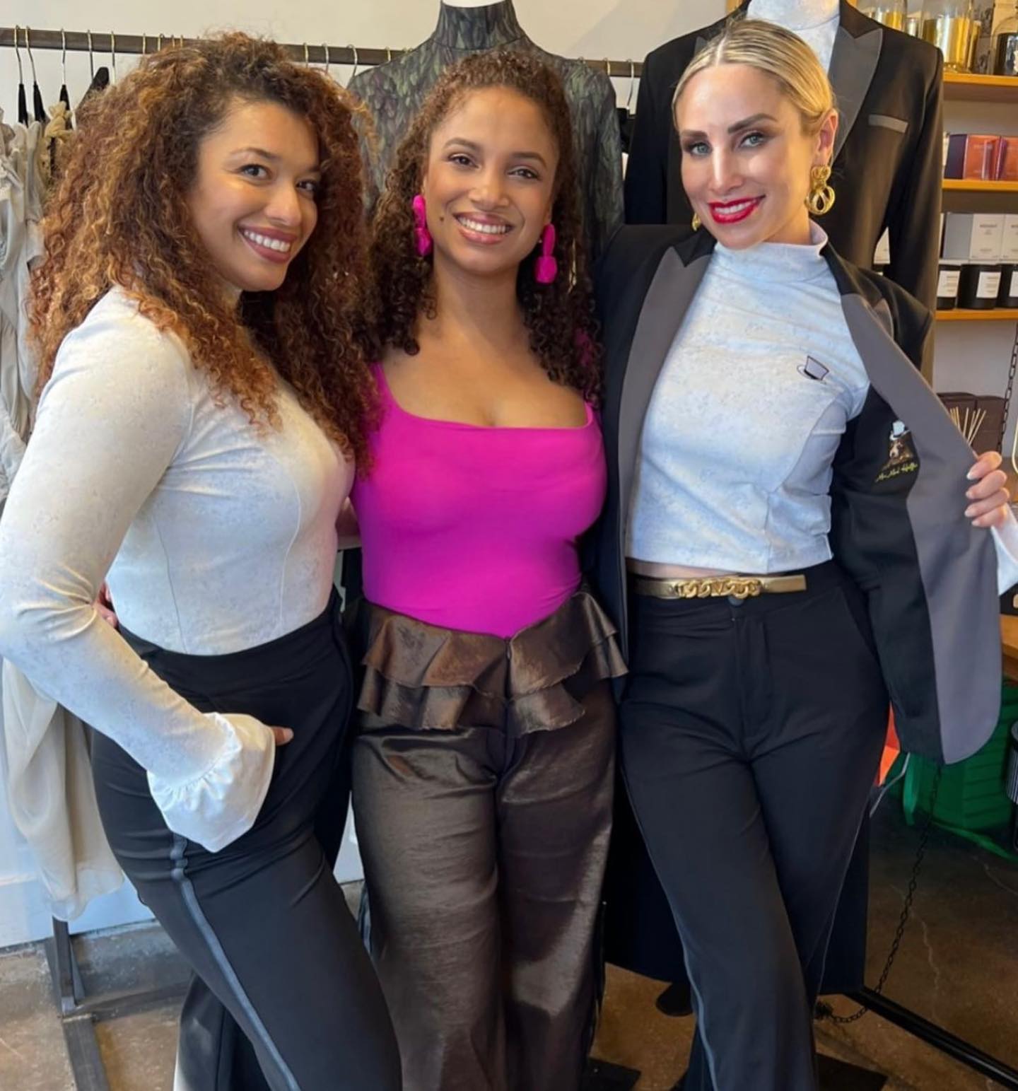 Three women posing together in stylish outfits, showcasing modern fashion in a boutique setting.