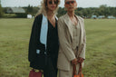 Two stylish women in fashionable suits, sunglasses, and handbags posing in a green field.