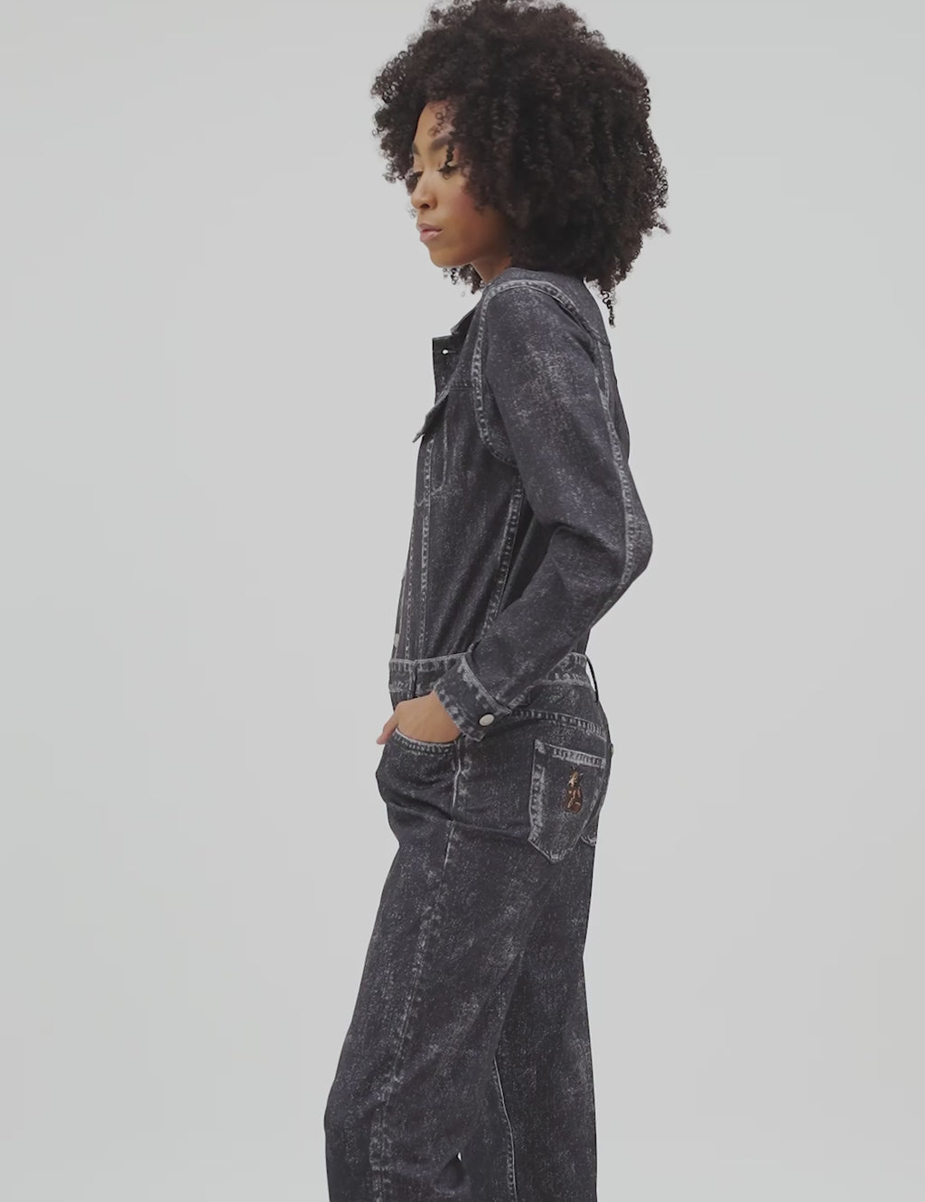 Model wearing a distressed dark denim jumpsuit with buttons, pockets, and relaxed fit.