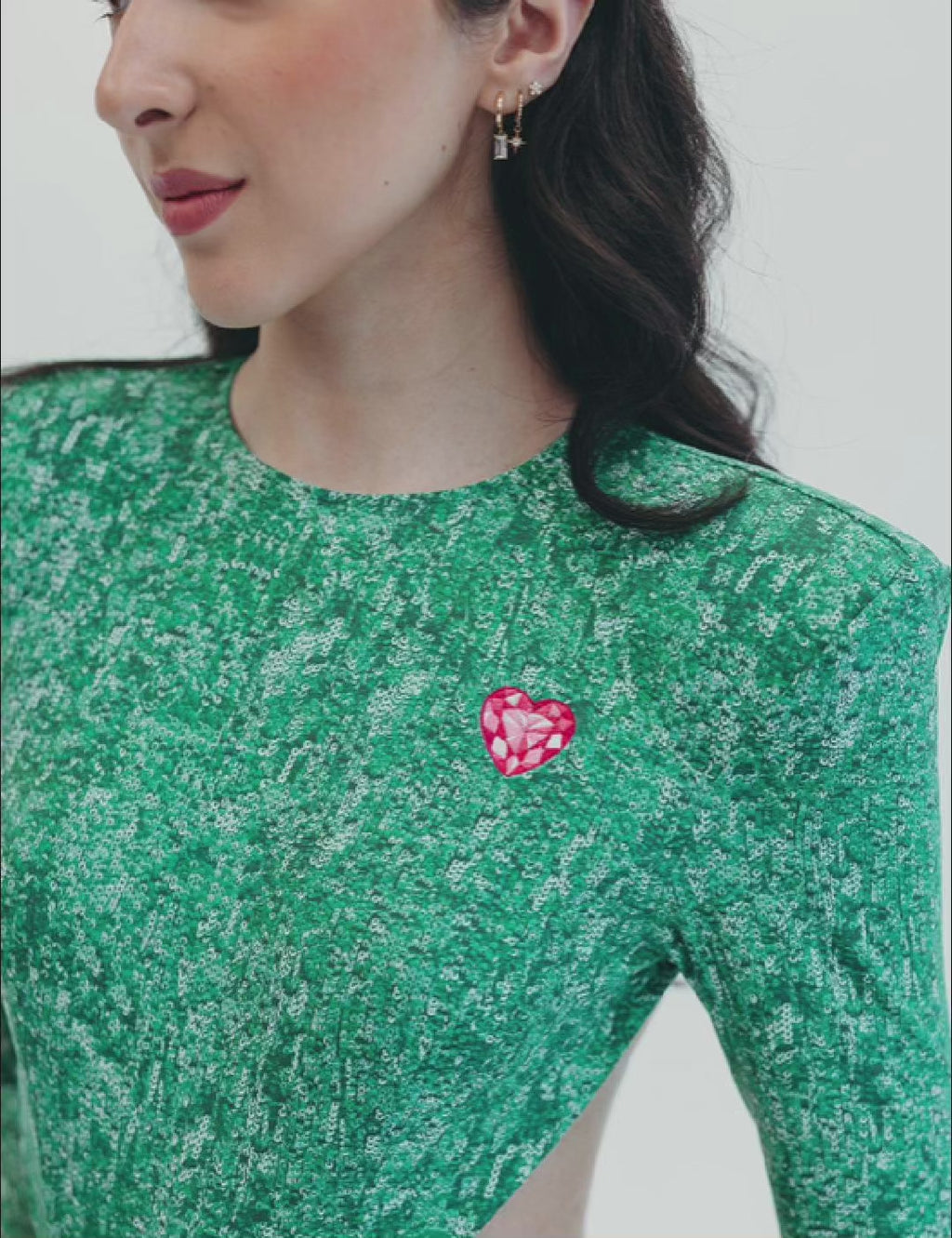 Model wearing the 'Verde Mi Amor' jumpsuit, showcasing green sequins, open back, and unique heart brooch detail.Model wearing the 'Verde Mi Amor' jumpsuit, showcasing green sequins, open back, and unique heart brooch detail.