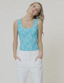 Model wearing a turquoise scoop neck tank bodysuit with white pants for a fresh, stylish look.