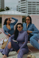 Three women in stylish outfits pose on the beach, showcasing a trendy summer vibe with sunglasses and chic attire.