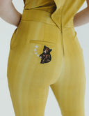 Back view of a yellow jumpsuit featuring a bear patch and star details on the pocket, highlighting unique design elements.