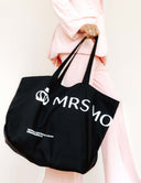 A person carrying The Marquee Tote bag in black with MRS MO logo, styled with a pink suit.