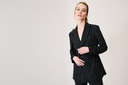 Confident model in a stylish black pinstriped suit on a neutral background, showcasing modern fashion elegance.